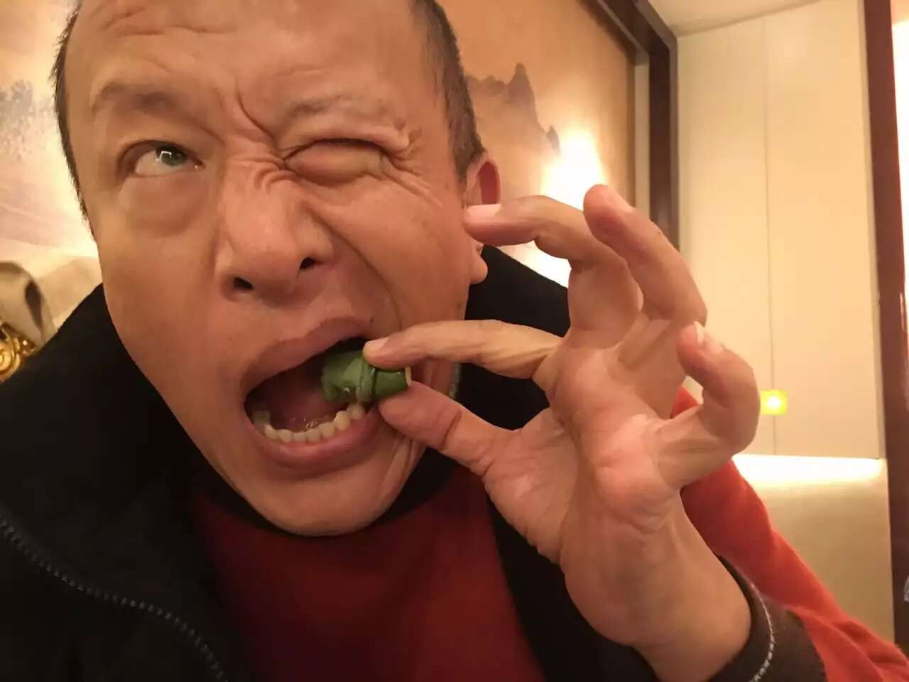 仁波切捏着绿叶包，张着嘴，一只眼睛挤紧。