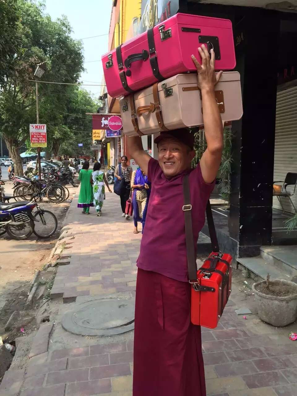 Rinpoche smiling with pink and cream cases stacked above his head and a small red case at his side.
