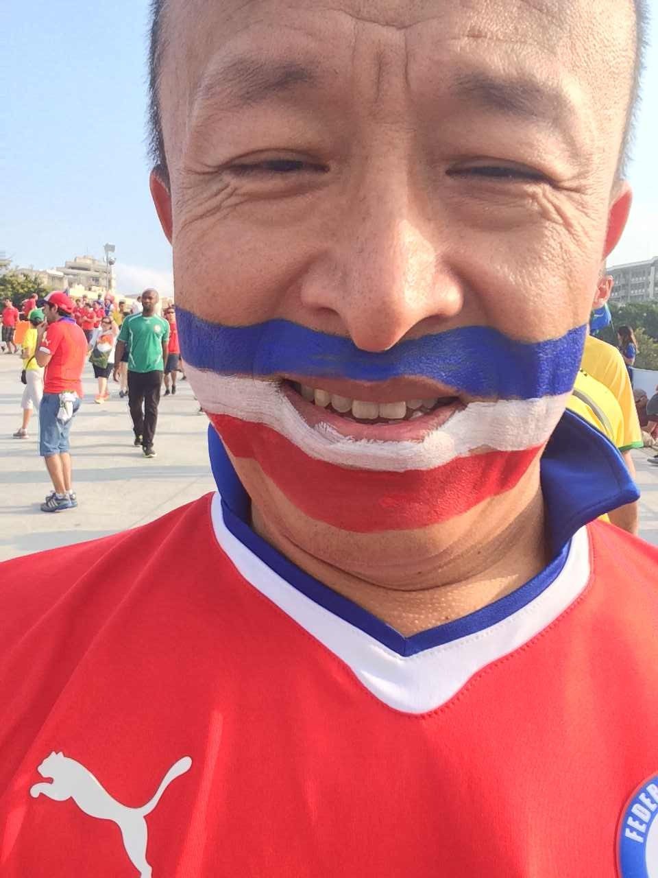 Rinpoche in a red football shirt, with blue, white and red painted across his cheeks and mouth.