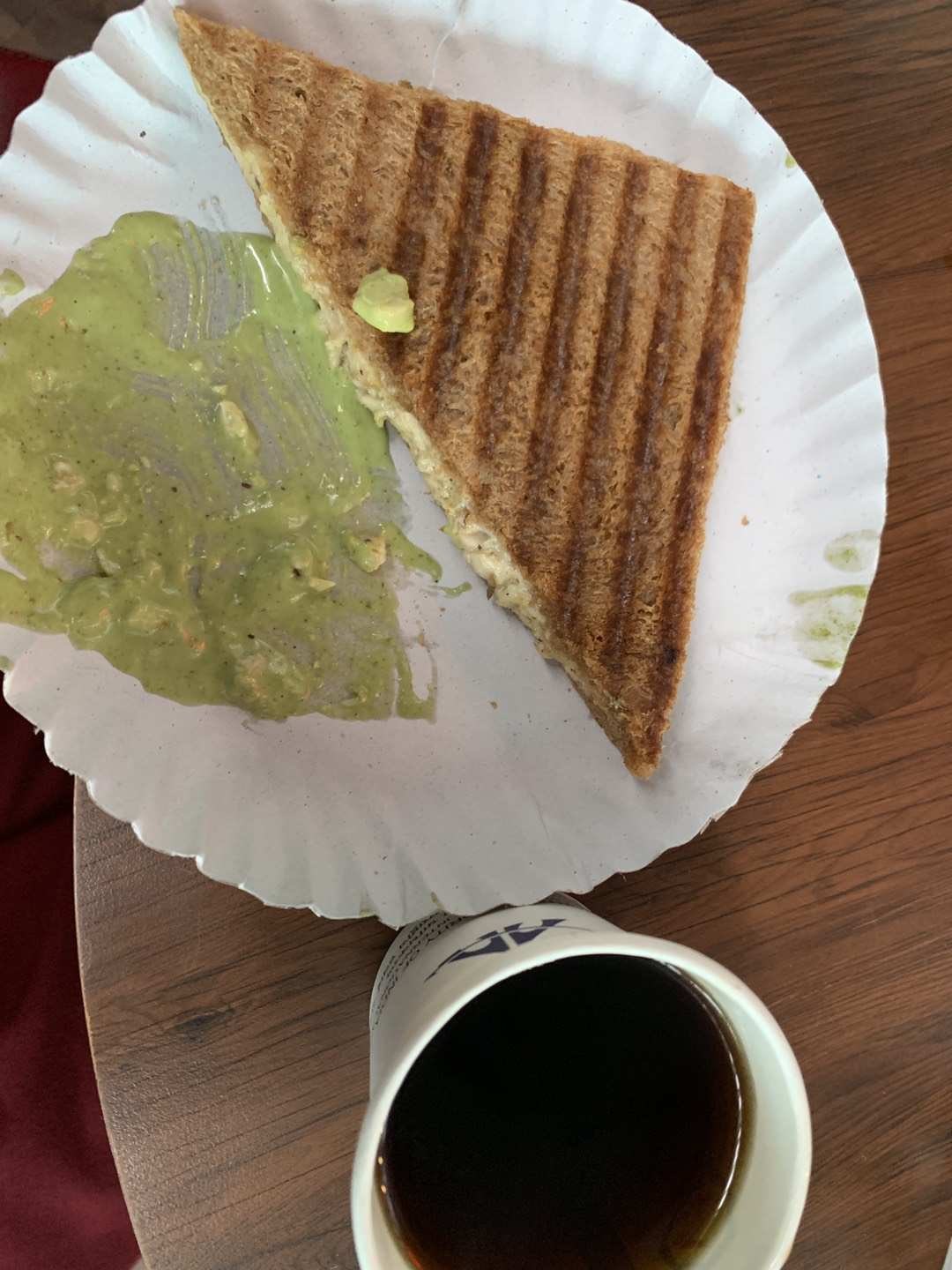 木桌上，三明治旁是一只纸杯。